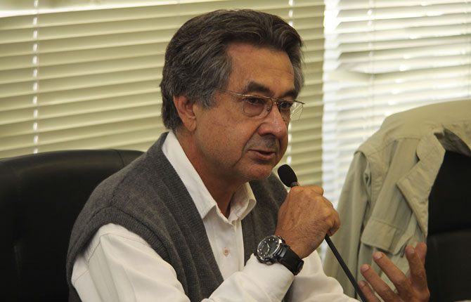 Descrição de Imagem: Fotografia do Dr. José Carlos do Carmo, conhecido como Kal. É um homem com cabelos curtos e grisalhos e usa óculos Ele está palestrando e segurando um microfone, vesta uma camisa branca de manga comprida e um colete de lá cinza.