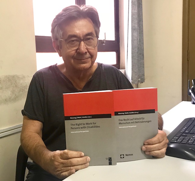 Na foto, Dr. José Carlos do Carmo, Kal, segura as duas edições do livro, uma escrita em Inglês e a outra em Alemão. Ele está sorrindo. As capas são nas cores vermelha, cinza e preto.