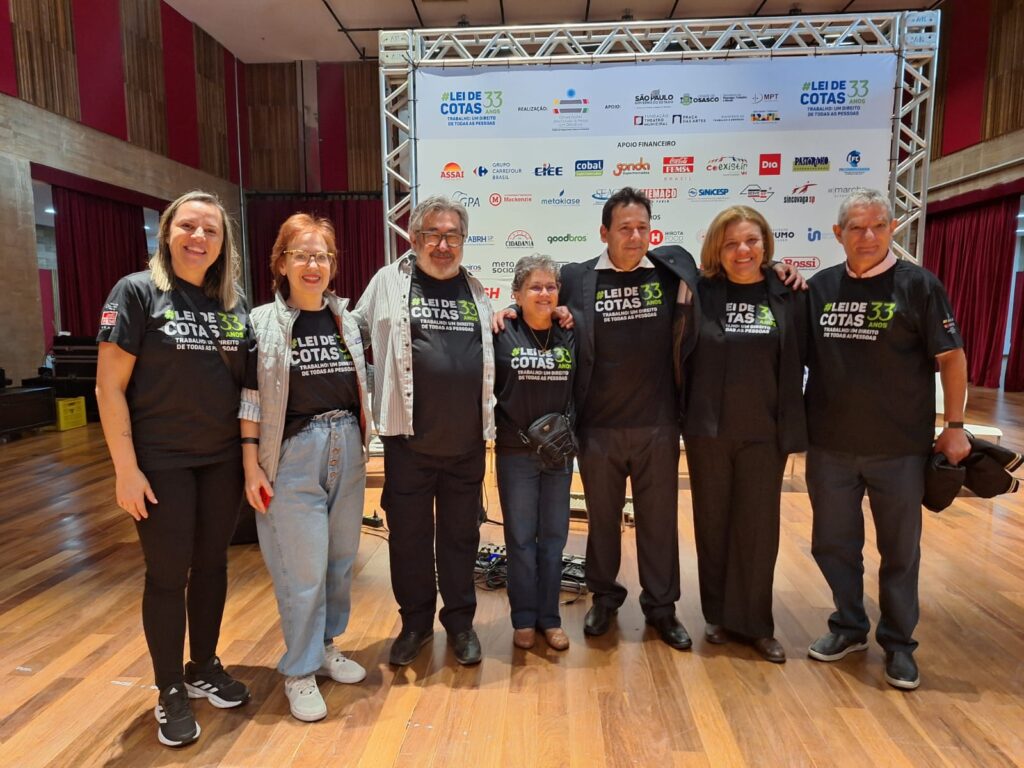 Fotos dos participantes presentes, em vários momentos. Grande parte das pessoas usa a camiseta preta com o texto: Lei de Cotas 33 anos, trabalho um direito de todas as pessoas.