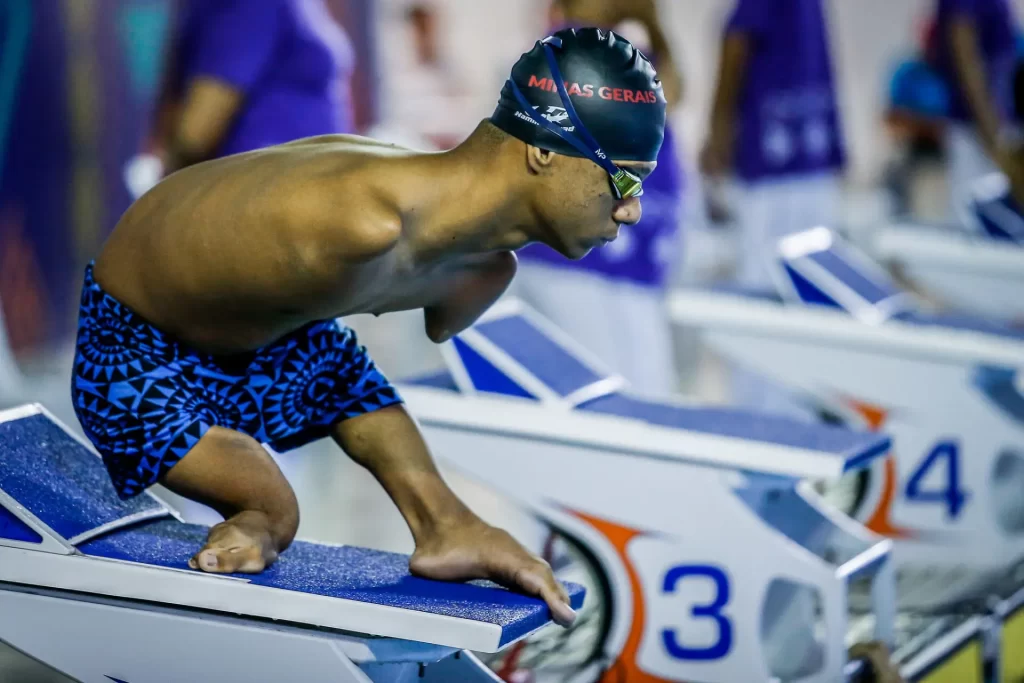 Gabriel Araújo em posição para saltar na piscina. Ele é negro, não tem os 2 braços e grande encurtamento das pernas.